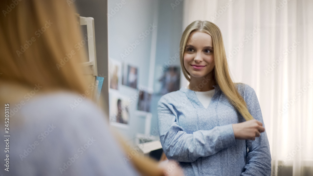 Smiling teen satisfied with soft and healthy hair, admiring her appearance