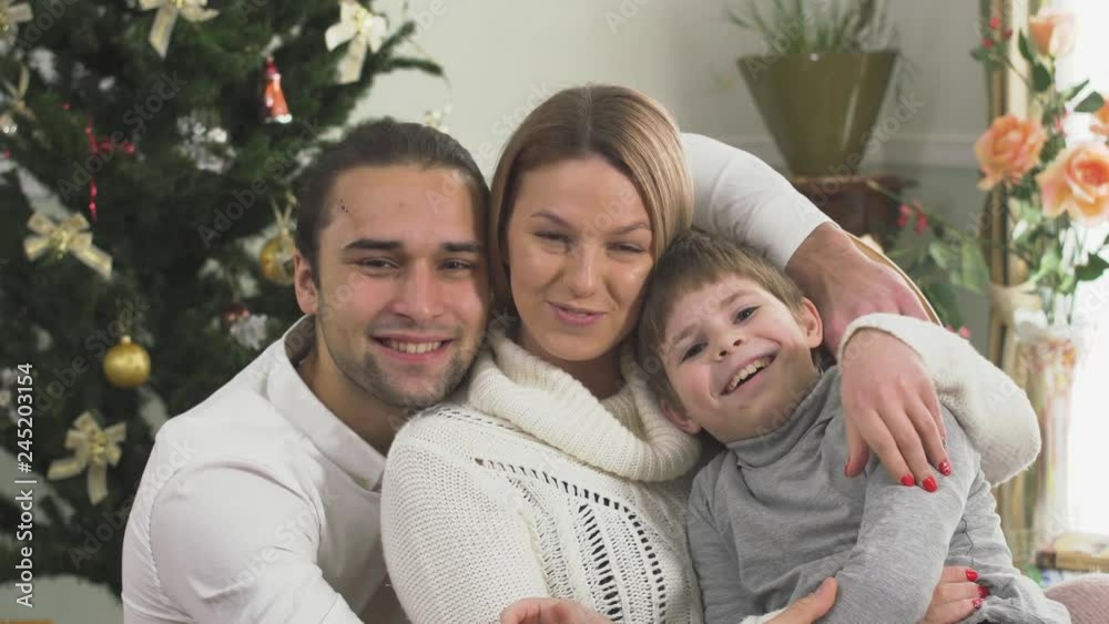 Portrait of joyful family sitting near Christmas tree at home together. Happy young family with child. Portrait of joyful family sitting near Christmas tree at home together. Happy young family with child.