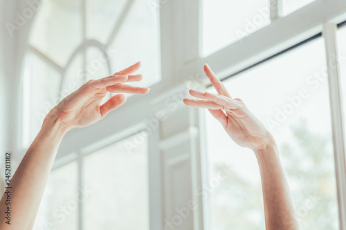 Young classical ballet dancer woman in dance class. Beautiful graceful ballerina practice ballet positions in blue tutu skirt near large window in white light hall. Hands close up photo