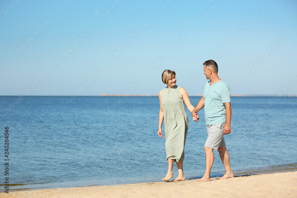 Happy mature couple holding hands at beach on sunny day