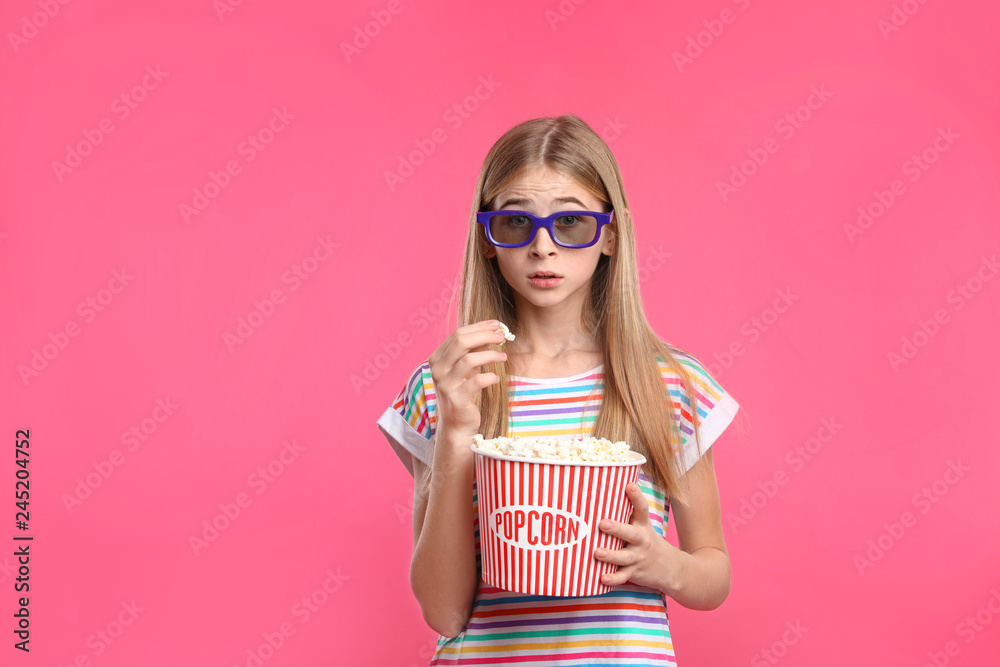 Fototapeta premium Emotional teenage girl with 3D glasses and popcorn during cinema show on color background