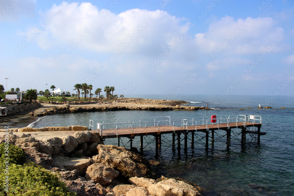 The rocky shore of the sea.In the distance the pier. Tide. Turquoise beautiful water. Blue sky. Cyprus, Paphos, Mediterranean sea.