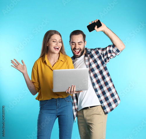 Emotional young people with laptop celebrating victory on color background