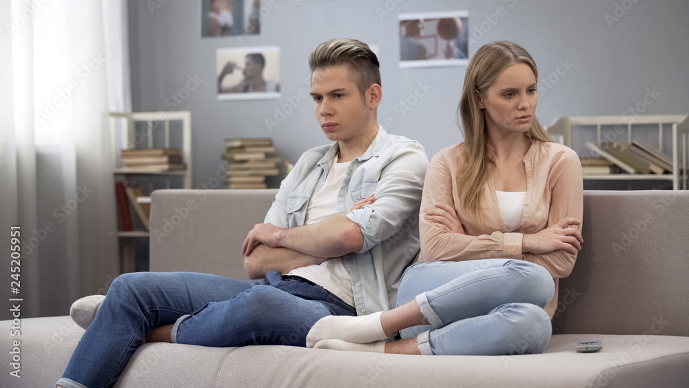Two angry teenagers sitting on couch turn way after quarrel, misunderstanding Two angry teenagers sitting on couch turn way after quarrel, misunderstanding