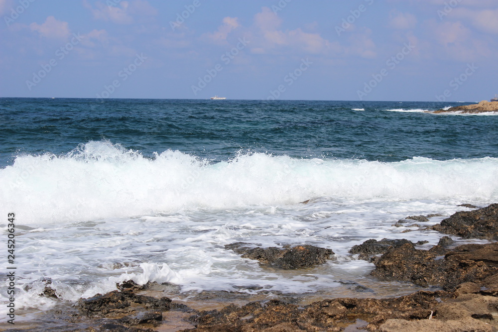 Rocky beach at low tide. Turquoise beautiful water. Restless waves. Clear blue sky. Cyprus, Paphos, Mediterranean sea.