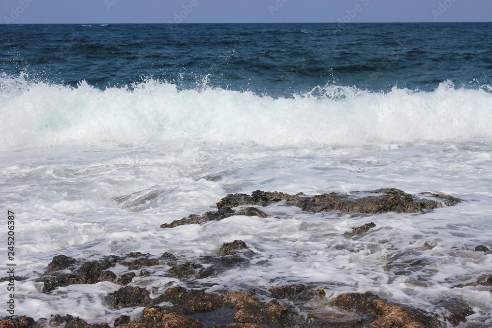 Rocky beach at low tide. Turquoise beautiful water. Restless waves. Clear blue sky. Cyprus, Paphos, Mediterranean sea.