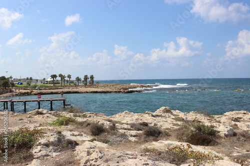 The rocky shore of the sea.In the distance the pier. Tide. Turquoise beautiful water. Blue sky. Cyprus  Paphos  Mediterranean sea.