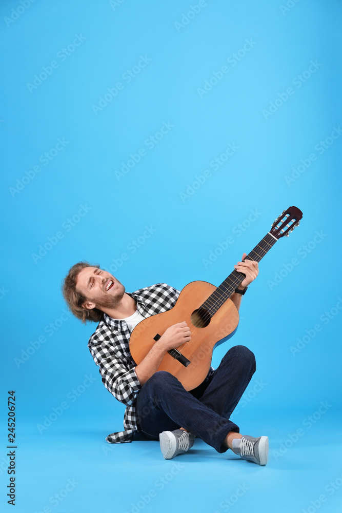 Young man playing acoustic guitar on color background