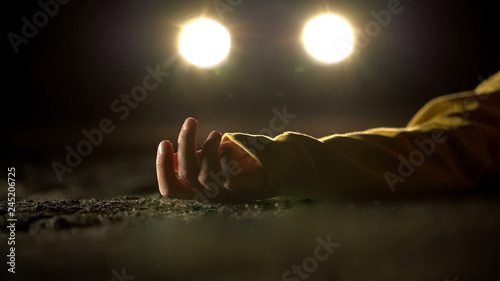 Car headlighting unconscious victim, lying on road after accident, crime