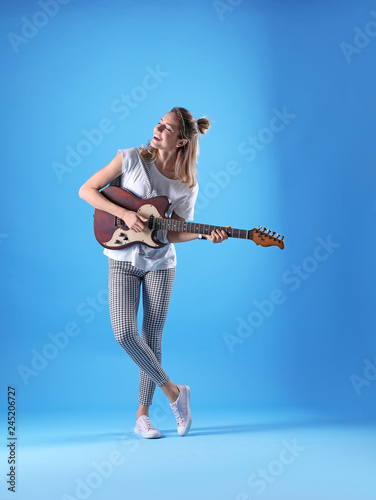 Young woman playing electric guitar on color background