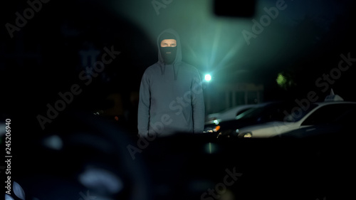Unrecognizable man in mask standing in front of car, threatening driver, crime © motortion