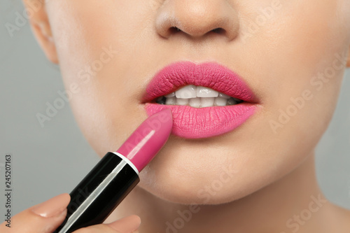 Young woman applying beautiful lipstick on gray background, closeup