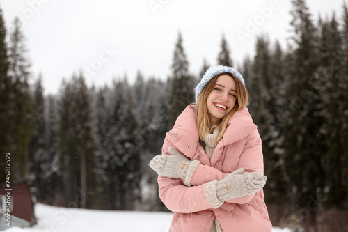 Young woman in warm clothes near forest, space for text. Winter vacation