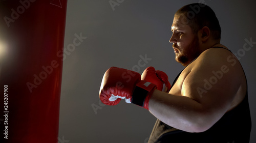 Heavyweight boxer practicing kicks with punching bag, champion training program