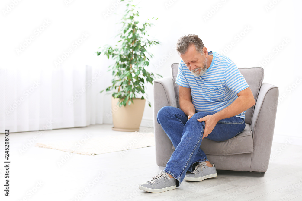 Senior man suffering from knee pain in living room. Space for text
