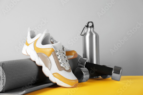 Composition of modern training shoes with mat, bottle and dumbbells on table