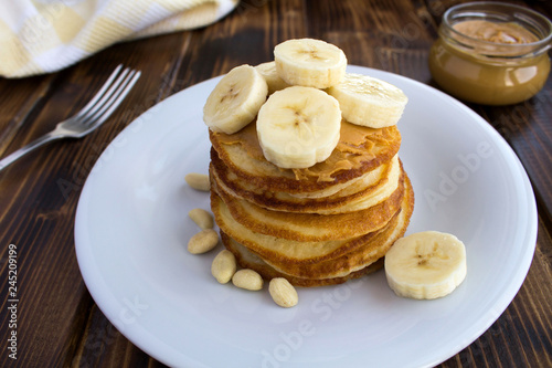 Homemade pancakes with peanut paste and banana in the white plate on the brown wooden background