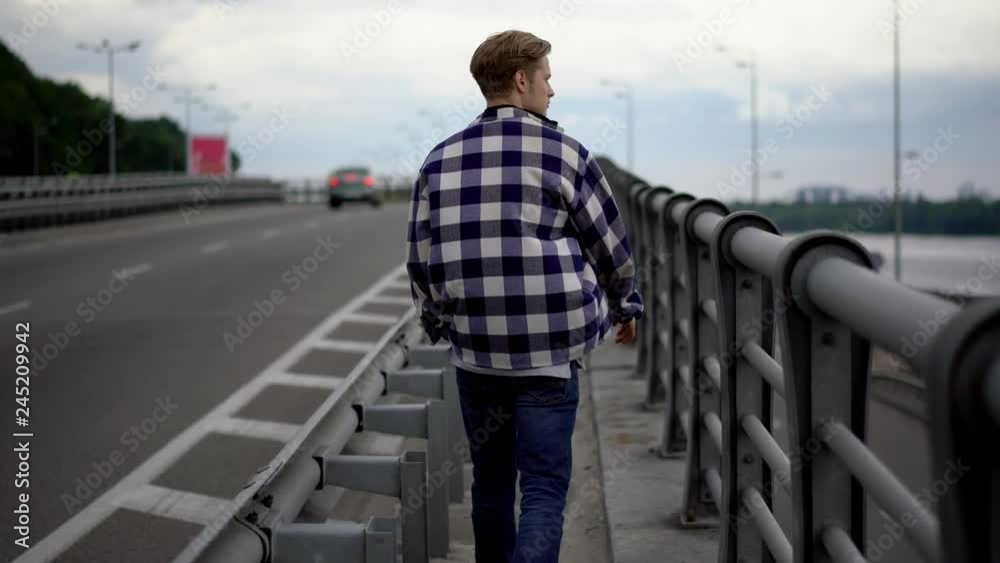 Young man walking along bridge Young man walking along bridge