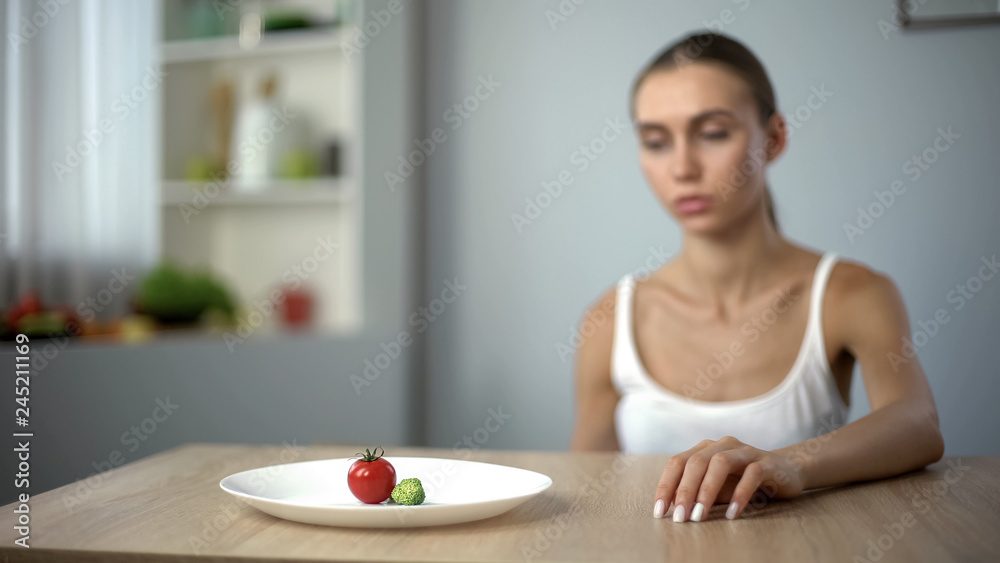 Exhausted slim woman looking at small portion of breakfast, self-destruction