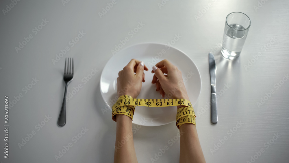 Fototapeta premium Hands tied with tapeline on empty plate, girl obsessed with counting calories
