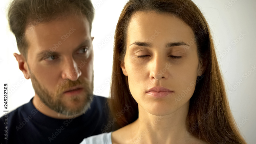 Man standing behind wife, sad lady with closed eyes hearing husband decisions Man standing behind wife, sad lady with closed eyes hearing husband decisions