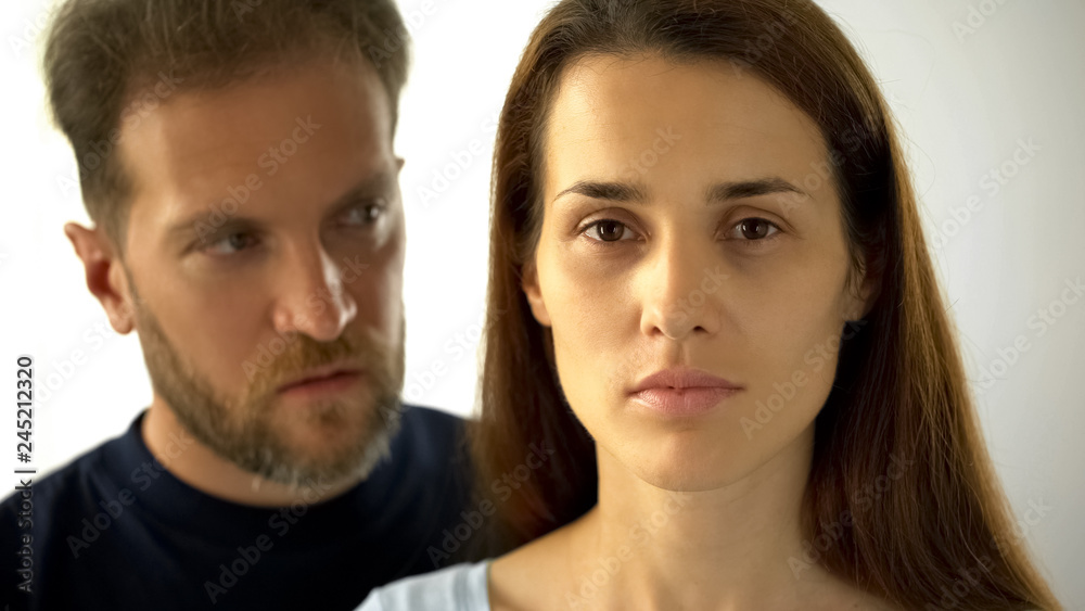 Pensive woman looking at camera man behind wife, inability to make own decisions Pensive woman looking at camera man behind wife, inability to make own decisions