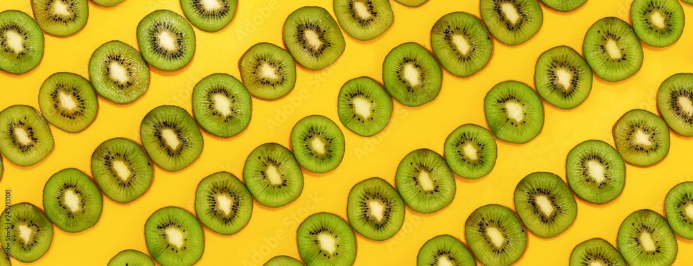 Green kiwifruit slices in lines with hard shadows on yellow background, flat lay image. Green kiwifruit slices in lines with hard shadows on yellow background, flat lay image.