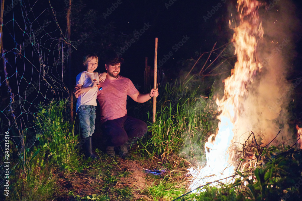Obraz premium father and son, villagers burning brushwood on fire at night, seasonal cleaning of the countryside area, village lifestyle
