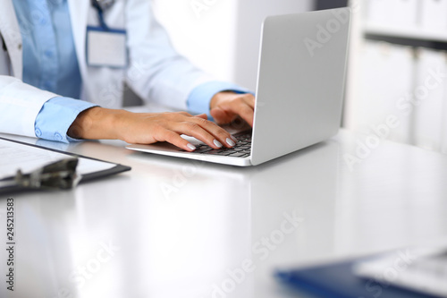 Unknown doctor woman typing on laptop computer while sitting at the desk in hospital office. close-up of hands. Physician at work. Medicine and health care concept