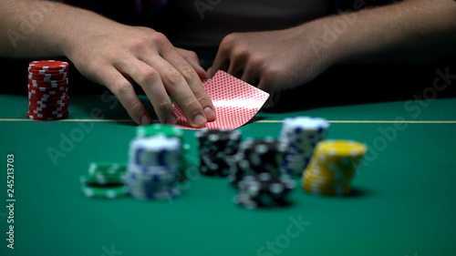 Man checking cards and raising, bluffing during poker tournament, chance to win