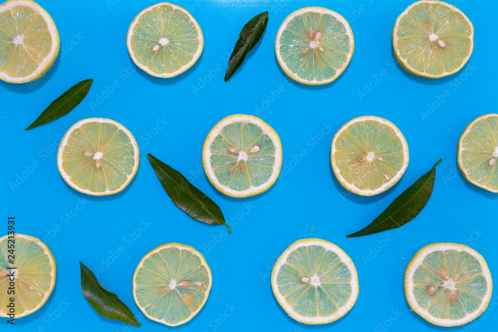 Lemon slices with leaves on blue background, flat lay image.
