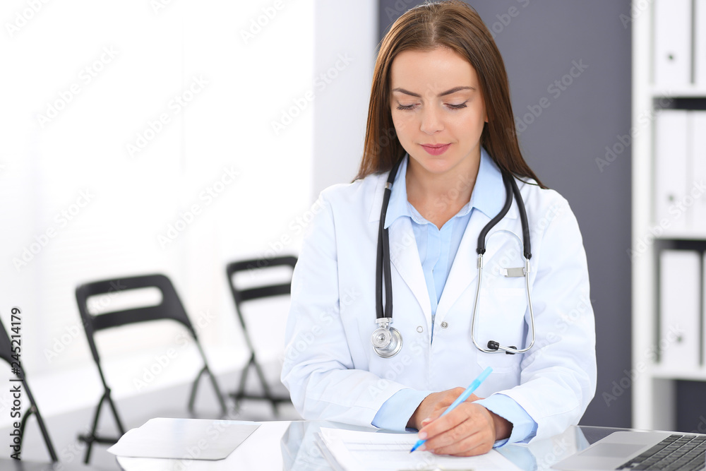 Doctor woman at work. Portrait of female physician filling up medical form while sitting at the glass desk at clinic or hospital. Medicine and healthcare concept Doctor woman at work. Portrait of female physician filling up medical form while sitting at the glass desk at clinic or hospital. Medicine and healthcare concept