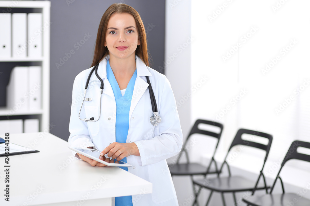 Doctor woman at work. Portrait of female physician using digital tablet  while standing near reception desk at clinic or emergency hospital. Medicine and healthcare concept