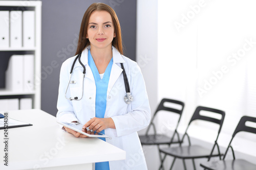 Doctor woman at work. Portrait of female physician using digital tablet while standing near reception desk at clinic or emergency hospital. Medicine and healthcare concept