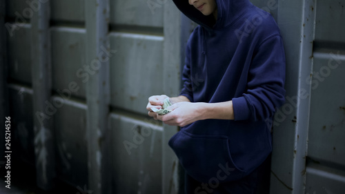 Poor boy secretly counting cash from pocket, poverty in beggar area, depression