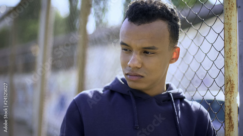 Young refugee from dysfunctional family leaning on fence, orphan teenager photo