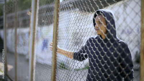 Migrant child separated from family, afro-american boy behind fence, detained photo