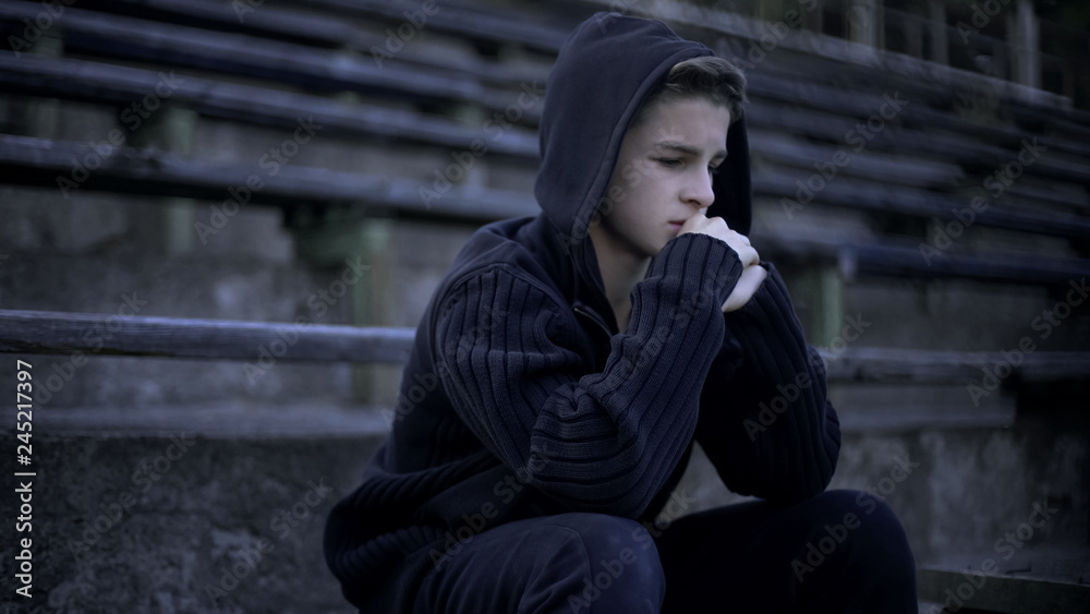 Upset boy sitting on stadium tribune, feels depression, loneliness and sorrow