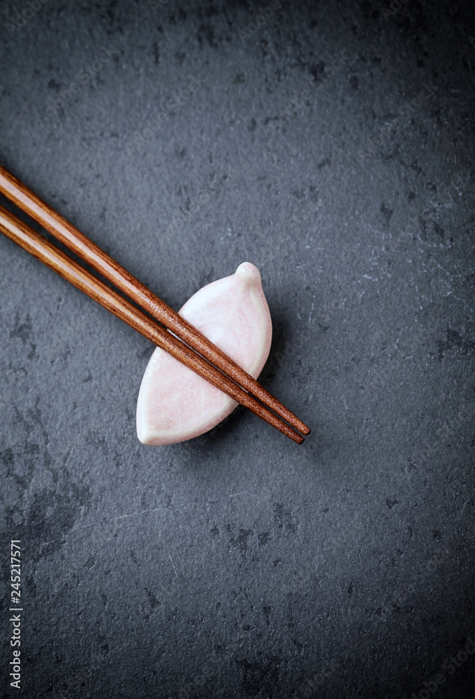 Wooden chopsticks and chopstick rest on black stone background. Top view. Copy space. Wooden chopsticks and chopstick rest on black stone background. Top view. Copy space.