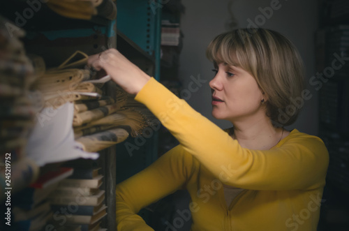 Librarian woman is looking for necessary newsletter article on a bookshelf in a archive of library. photo