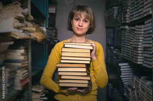 Foto Skeptical librarian holding in hands a stack of books in the library
