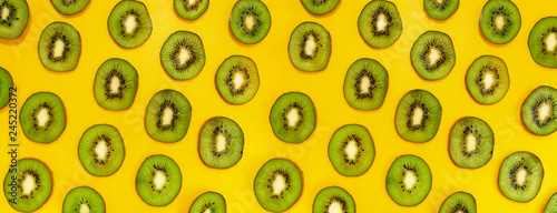 Green kiwifruit slices in lines with hard shadows on yellow background, flat lay image.