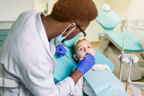 Teeth checkup at dentist s office. African-American dentist examining boy s teeth in the dentists chair