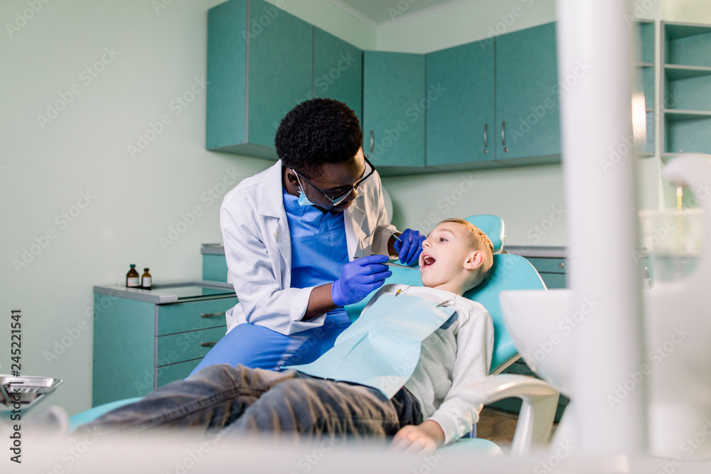 Young beautiful boy in dental office. Children's African-American dentist examines teeth to a child. Young beautiful boy in dental office. Children's African-American dentist examines teeth to a child.