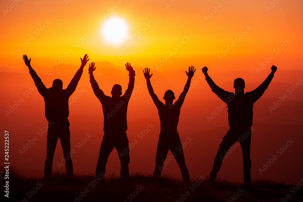 Silhouette group of hikers greetings sun with raised hands against sunset. Hikers walking on a mountain at sunset. Silhouette group of hikers greetings sun with raised hands against sunset. Hikers walking on a mountain at sunset.