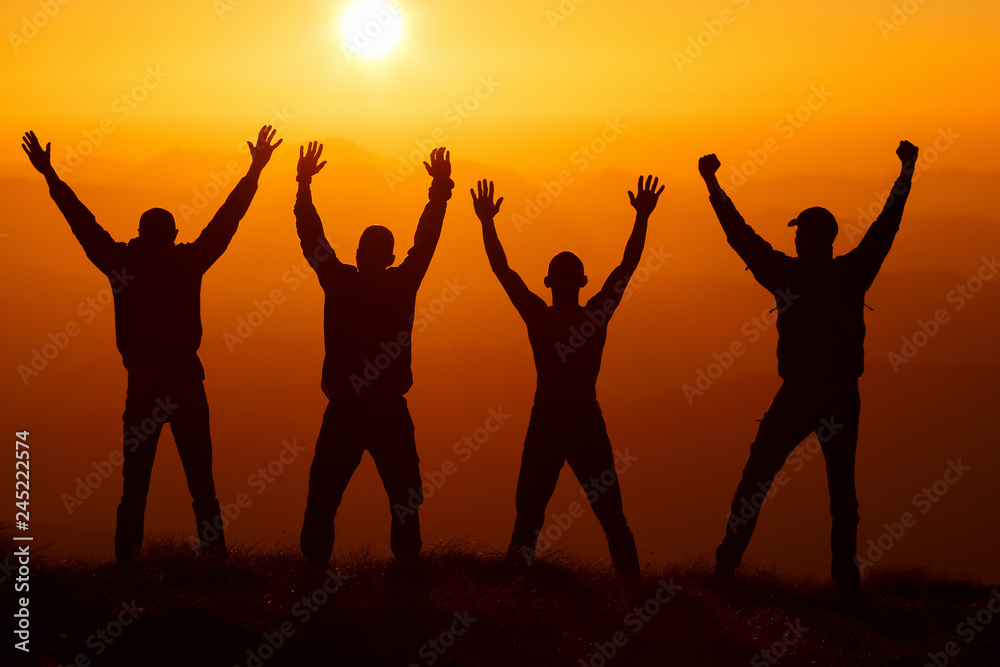 Silhouette group of hikers greetings sun with raised hands against sunset. Hikers walking on a mountain at sunset.