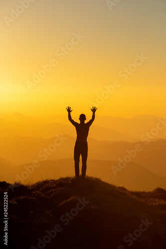 Man silhouette standing with hands up achieving the top. Hiker welcomes a sun. Tourist open arms on sunrise mountain top © Serhii