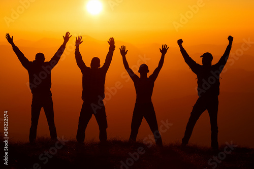 Silhouette group of hikers greetings sun with raised hands against sunset. Hikers walking on a mountain at sunset. © Serhii