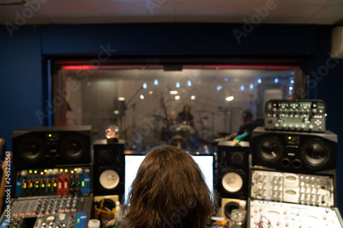 Music Engineer in Music Recording studio at mixing consol recording hip hop music viewing artists through glass