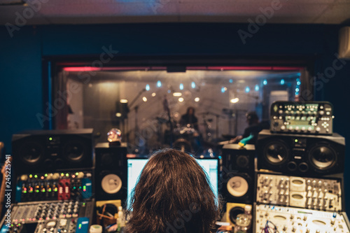 Music Engineer in Music Recording studio at mixing consol recording hip hop music viewing artists through glass